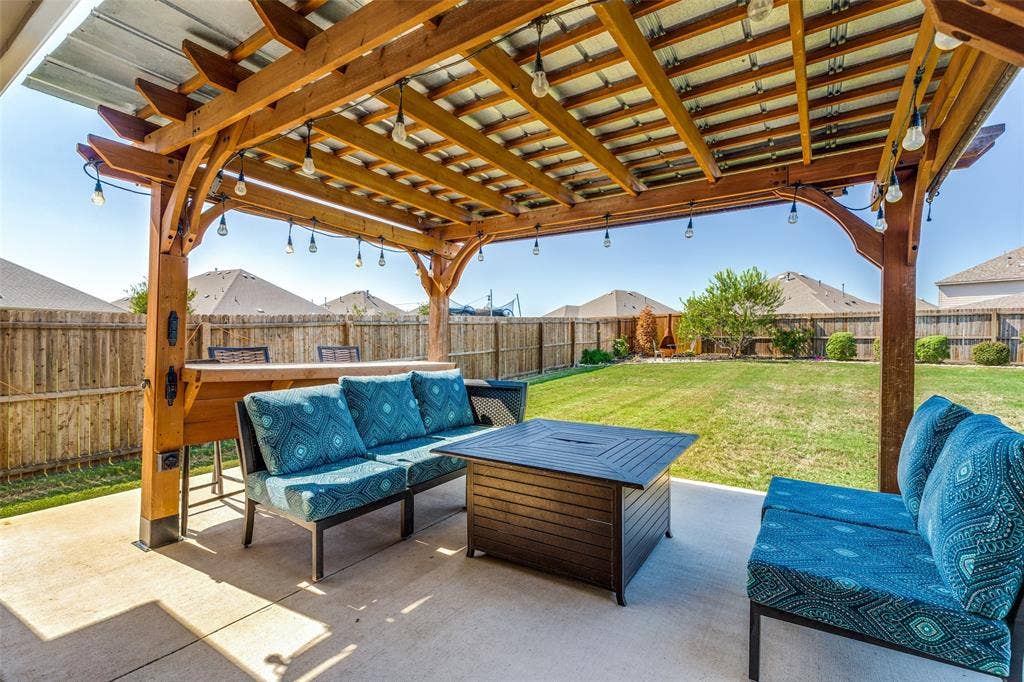 Expansive concrete patio with a wooden pergola featuring a metal roof and string lighting