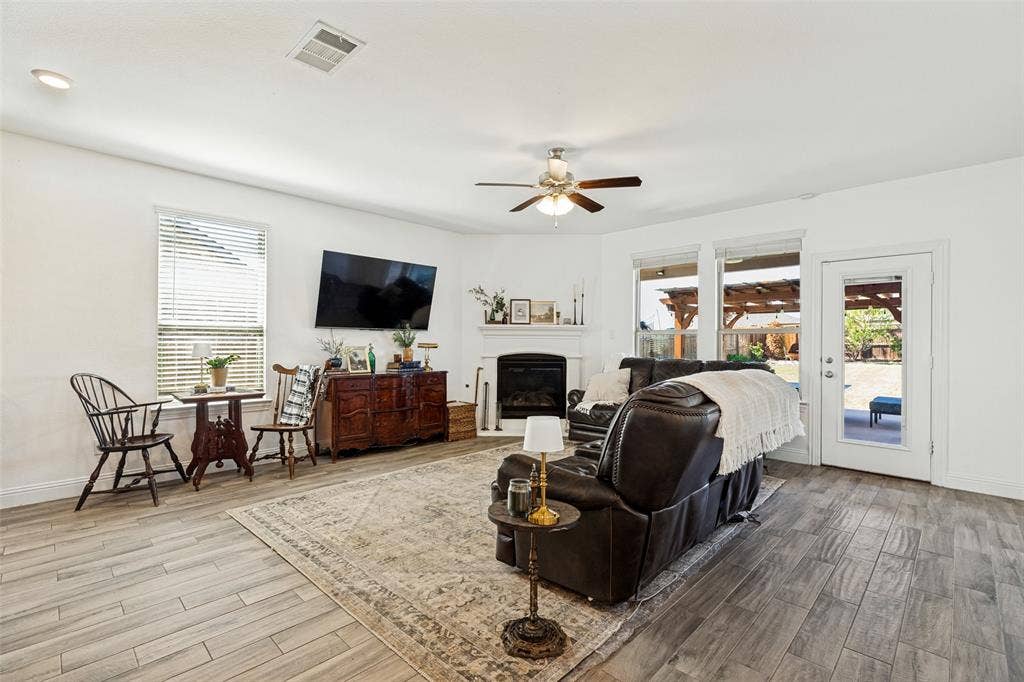 Bright interior featuring wood-finish flooring, a white fireplace with a mantel, and a ceiling fan