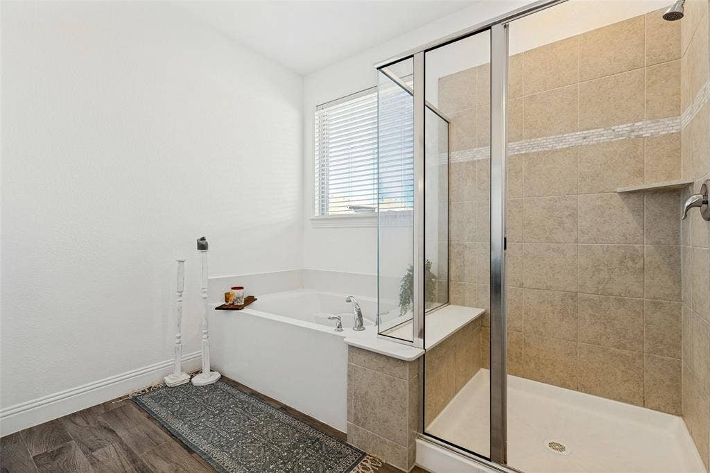 Soaking tub with a window, glass-enclosed shower, tile-surround shower, and wood-finish flooring