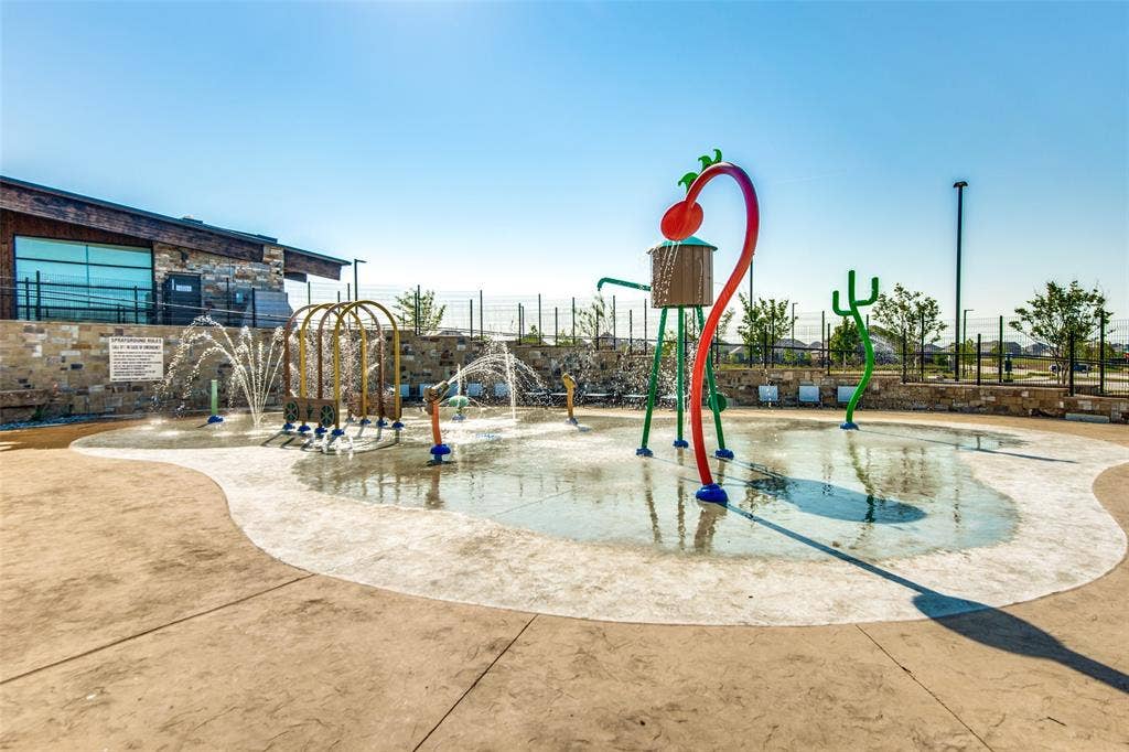 Splash pad with multiple water features, surrounded by a concrete surface and a stone-clad building