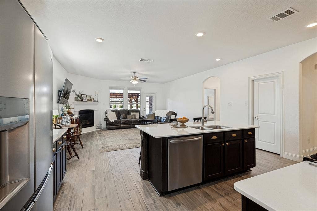Open-concept living space featuring wood-finish flooring, recessed lighting, and a kitchen island with a stainless steel sink and dishwasher