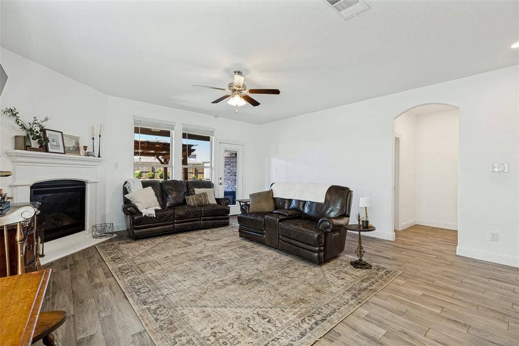 Living area featuring a fireplace with a white mantel, wood-finish flooring, multiple windows, and an arched doorway