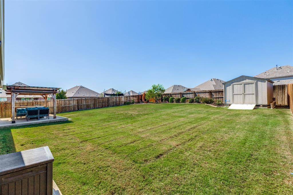 Expansive backyard with a large grassy area, a wooden privacy fence, a detached shed, and a paved patio area