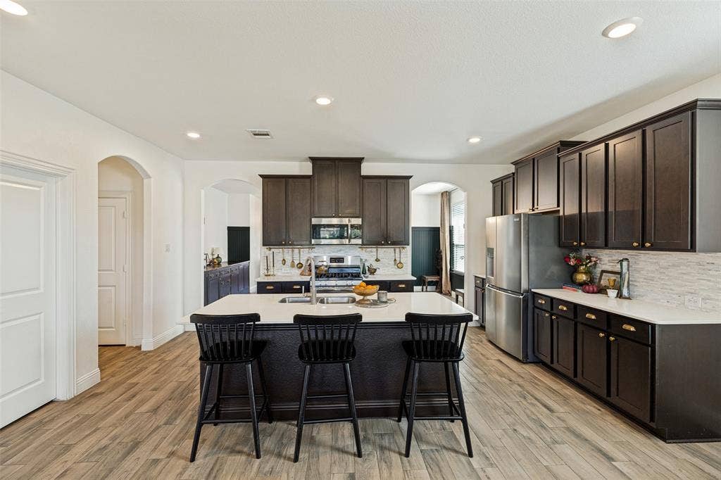 Kitchen featuring wood-finish flooring, dark wood cabinetry, stainless steel appliances, a center island with a light-colored countertop, and recessed lighting