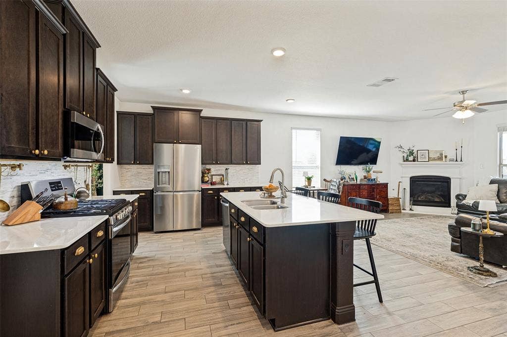 Gourmet kitchen featuring dark wood cabinetry, stainless steel appliances, a center island with sink, and wood-finish flooring