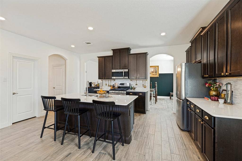 Chef's kitchen showcasing dark wood cabinetry, stainless steel appliances, white quartz countertops, and a large center island with seating