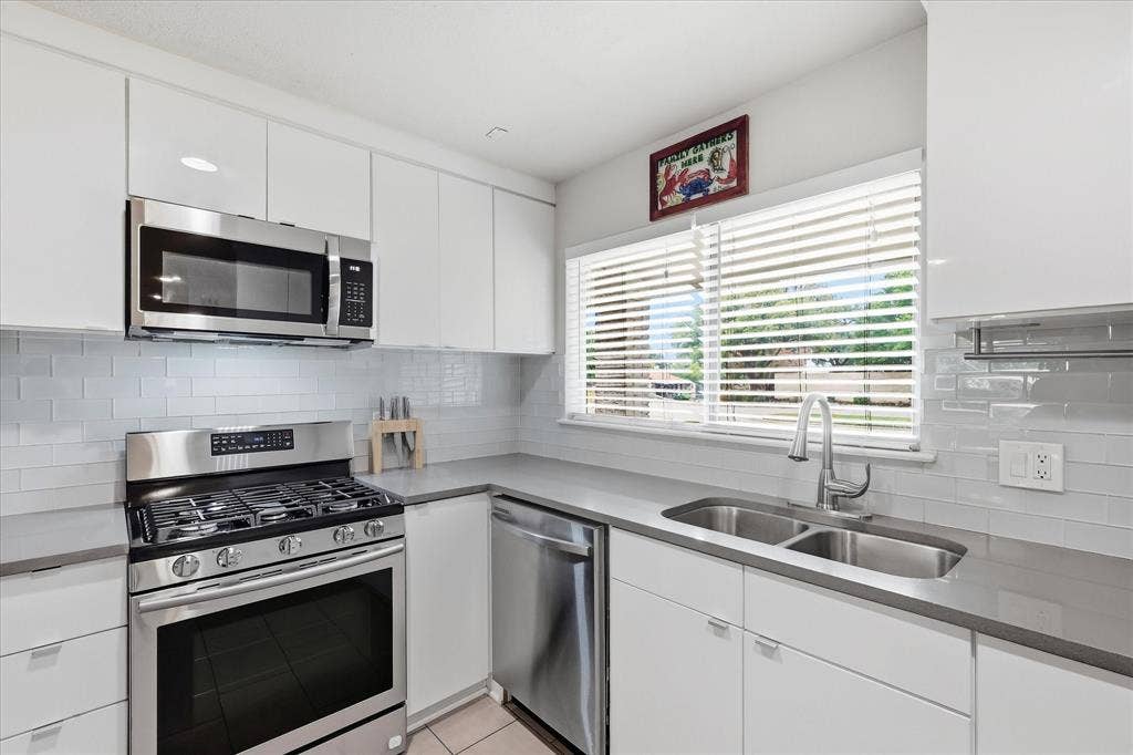 306 W Northgate Drive, Irving, TX 75062 Kitchen featuring white cabinetry, gray quartz countertops, stainless steel appliances, a subway tile backsplash, and a double basin sink