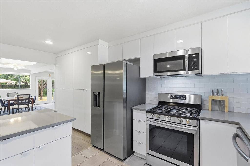 306 W Northgate Drive, Irving, TX 75062 Contemporary kitchen featuring white cabinetry, stainless steel appliances, gray quartz countertops, subway tile backsplash, and recessed lighting