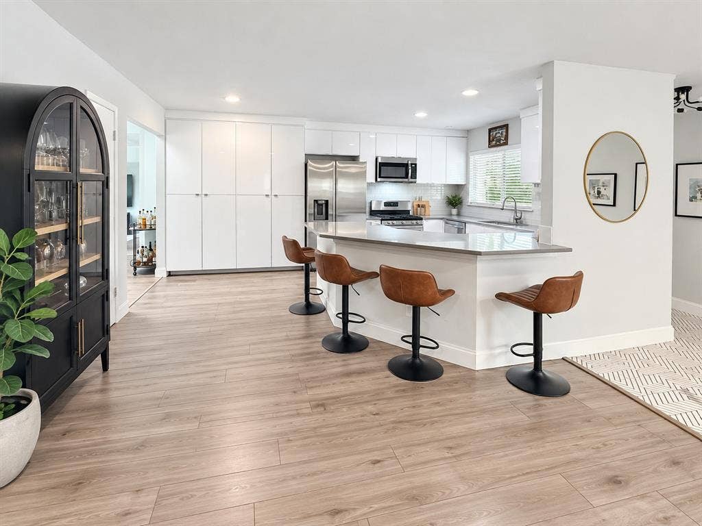 306 W Northgate Drive, Irving, TX 75062 Kitchen featuring a multi-functional island with a countertop, stainless steel appliances, white cabinetry, and wood-finish flooring