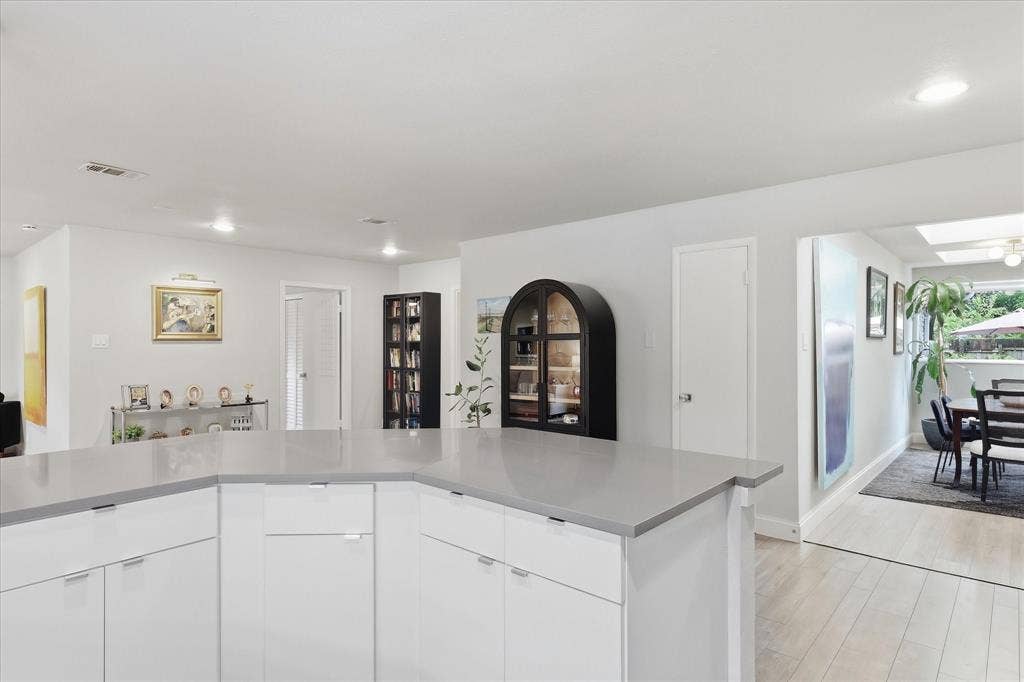 306 W Northgate Drive, Irving, TX 75062 Modern kitchen featuring white cabinetry with stainless steel hardware, gray quartz countertops, and light wood-finish flooring