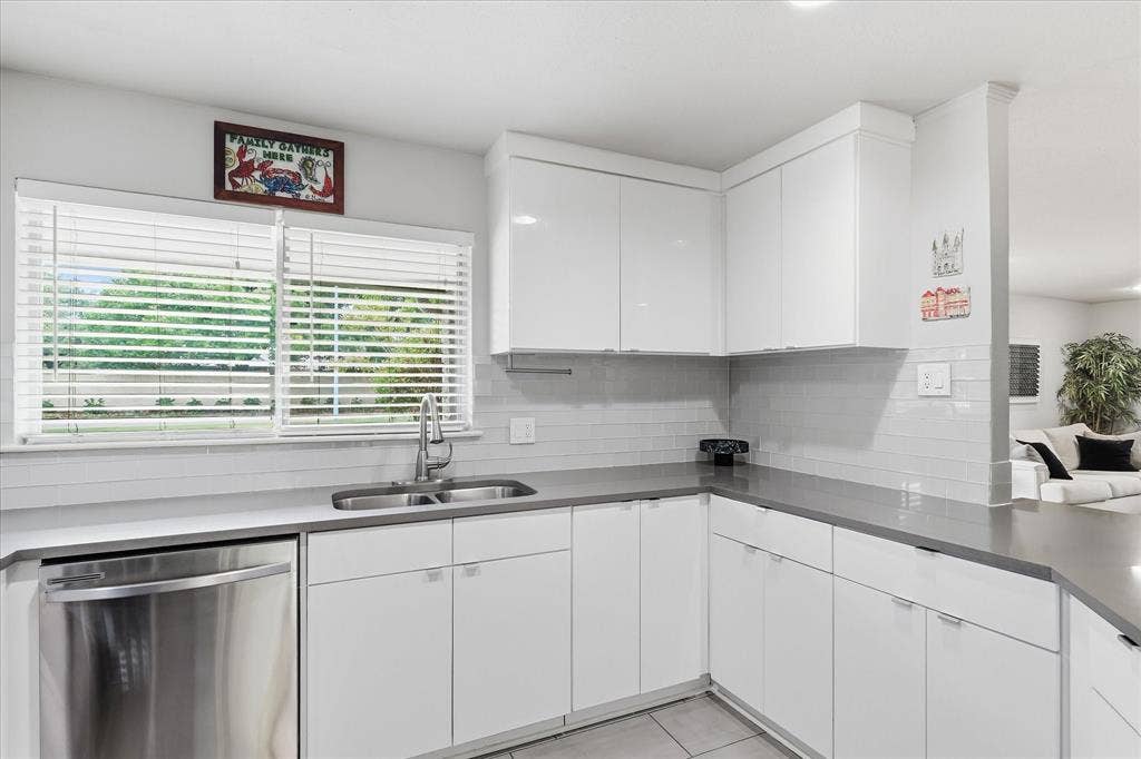 306 W Northgate Drive, Irving, TX 75062 White flat-panel cabinetry, stainless steel dishwasher, undermount double-basin sink, gray quartz countertops, and white subway tile backsplash