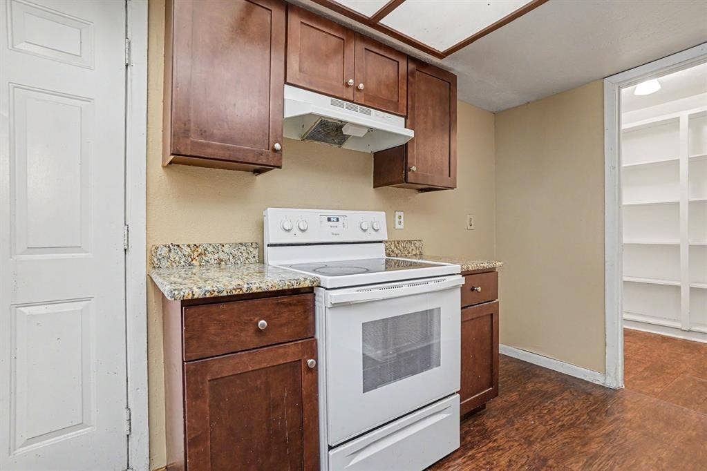 1414 Finley Road, Irving, TX 75062 Kitchen featuring wood-finish cabinetry, granite-style countertops, an electric range, and a built-in pantry with shelving