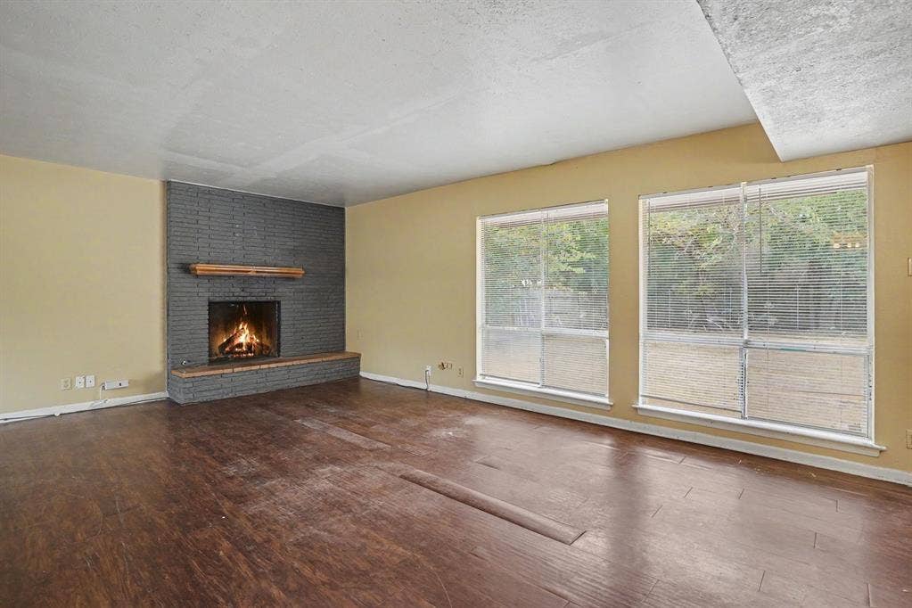 1414 Finley Road, Irving, TX 75062 Spacious room featuring wood-finish flooring, a brick-surround fireplace with a wood mantle, and two large windows