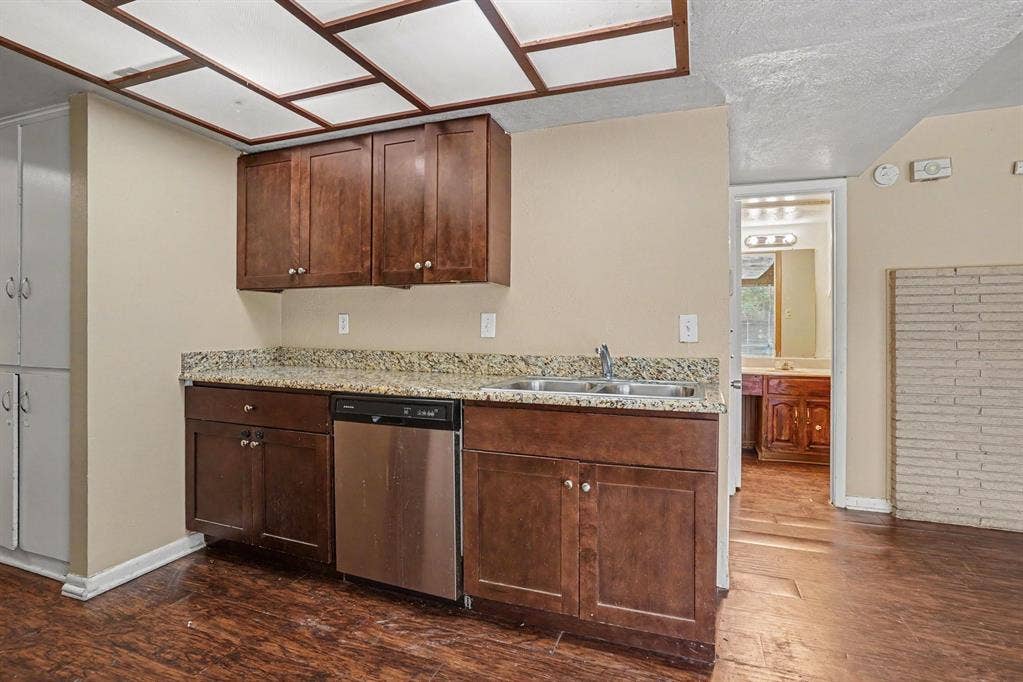 1414 Finley Road, Irving, TX 75062 Kitchenette featuring dark wood cabinetry, granite-style countertops, stainless steel dishwasher, and a double basin sink