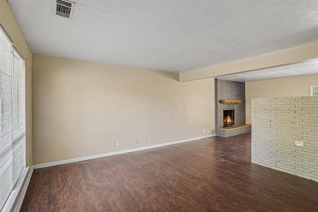 1414 Finley Road, Irving, TX 75062 Spacious living area featuring wood-finish flooring, a full-height brick fireplace with a wood mantel, and large windows