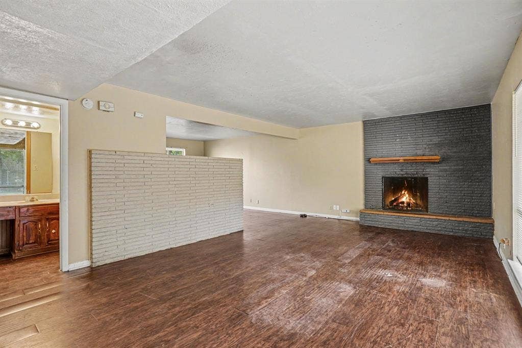 1414 Finley Road, Irving, TX 75062 Spacious living area featuring a dark brick fireplace with a wood mantle, wood-finish flooring, and a half-wall partition