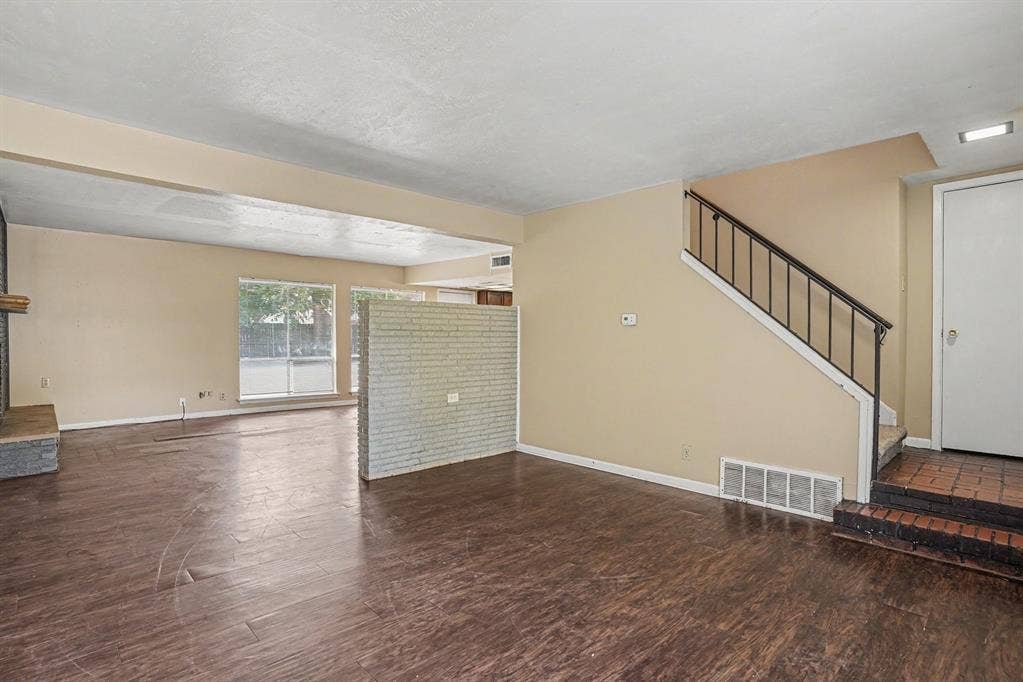 1414 Finley Road, Irving, TX 75062 Wood-finish flooring throughout, brick accent partition, fireplace with stone surround, large window with outdoor visibility, and a staircase with wrought iron railing