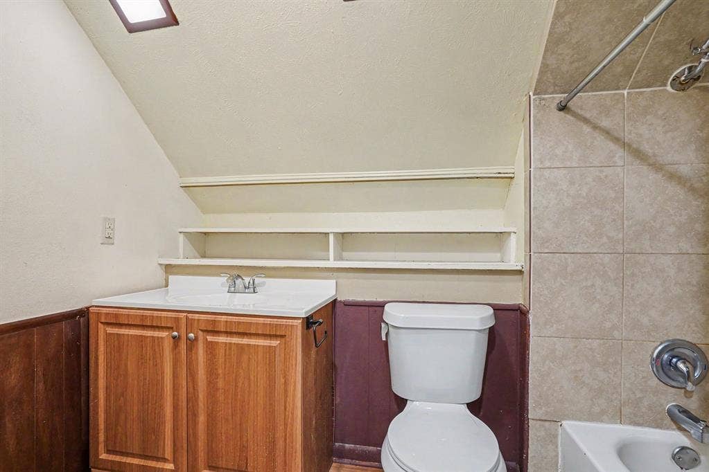 1414 Finley Road, Irving, TX 75062 White vanity countertop, wood-finish vanity cabinetry, built-in shelving, tiled shower surround, and a skylight
