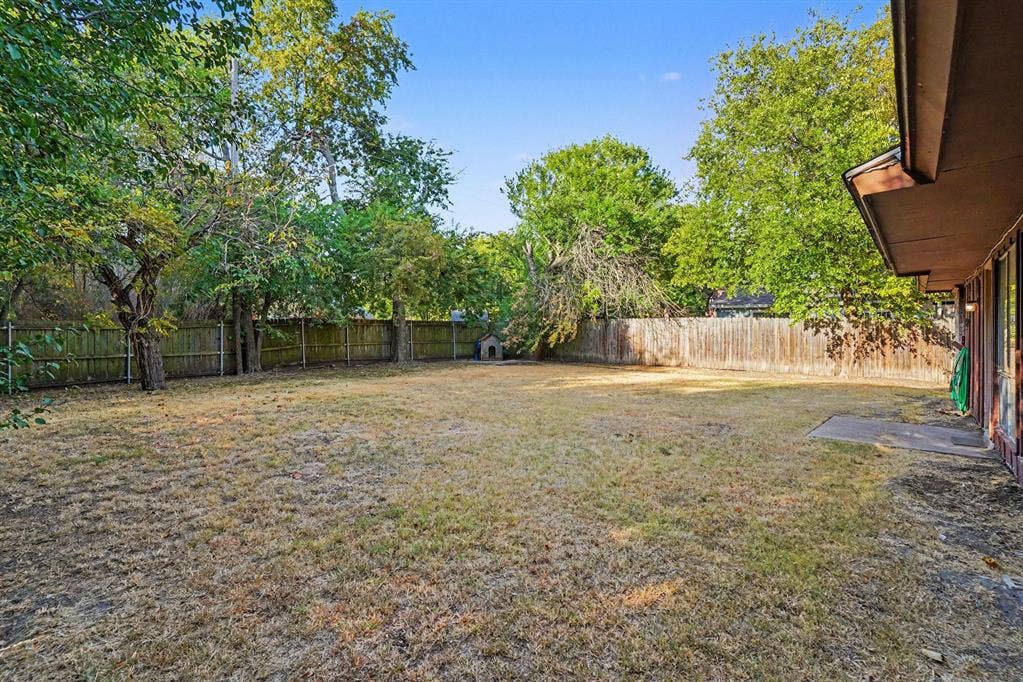 1414 Finley Road, Irving, TX 75062 Expansive backyard featuring a wood fence, mature trees, and a concrete patio
