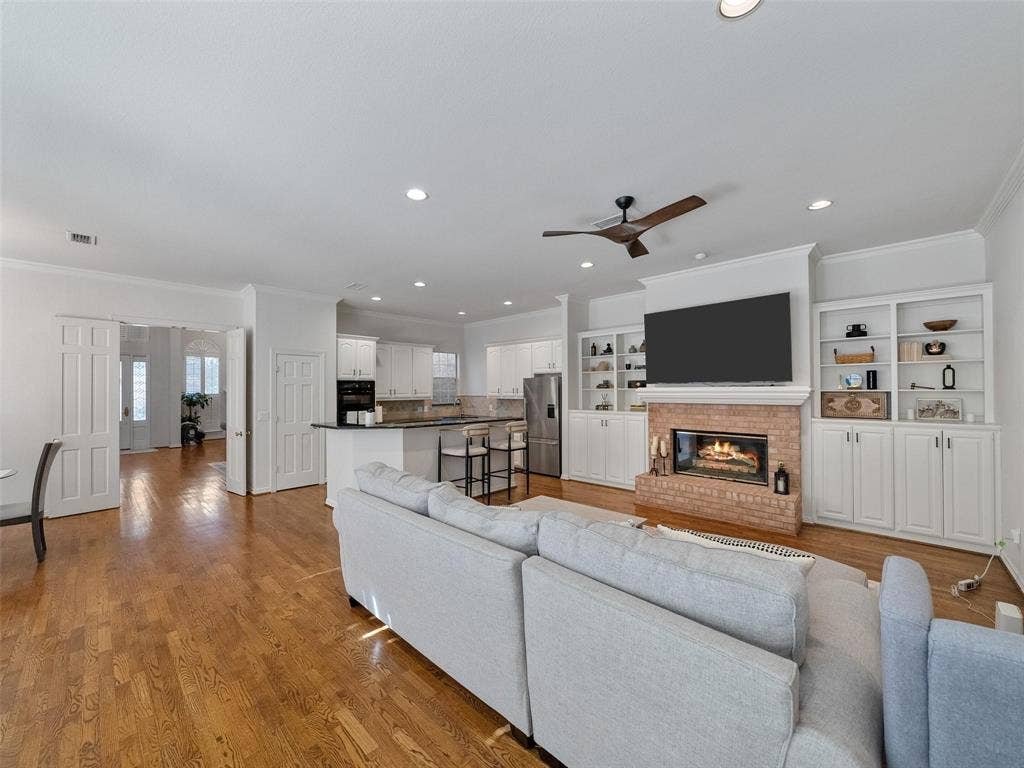 8640 Breakers Point, Dallas, TX 75243 Hardwood flooring, brick fireplace with mantel, built-in shelving, recessed lighting, and a ceiling fan