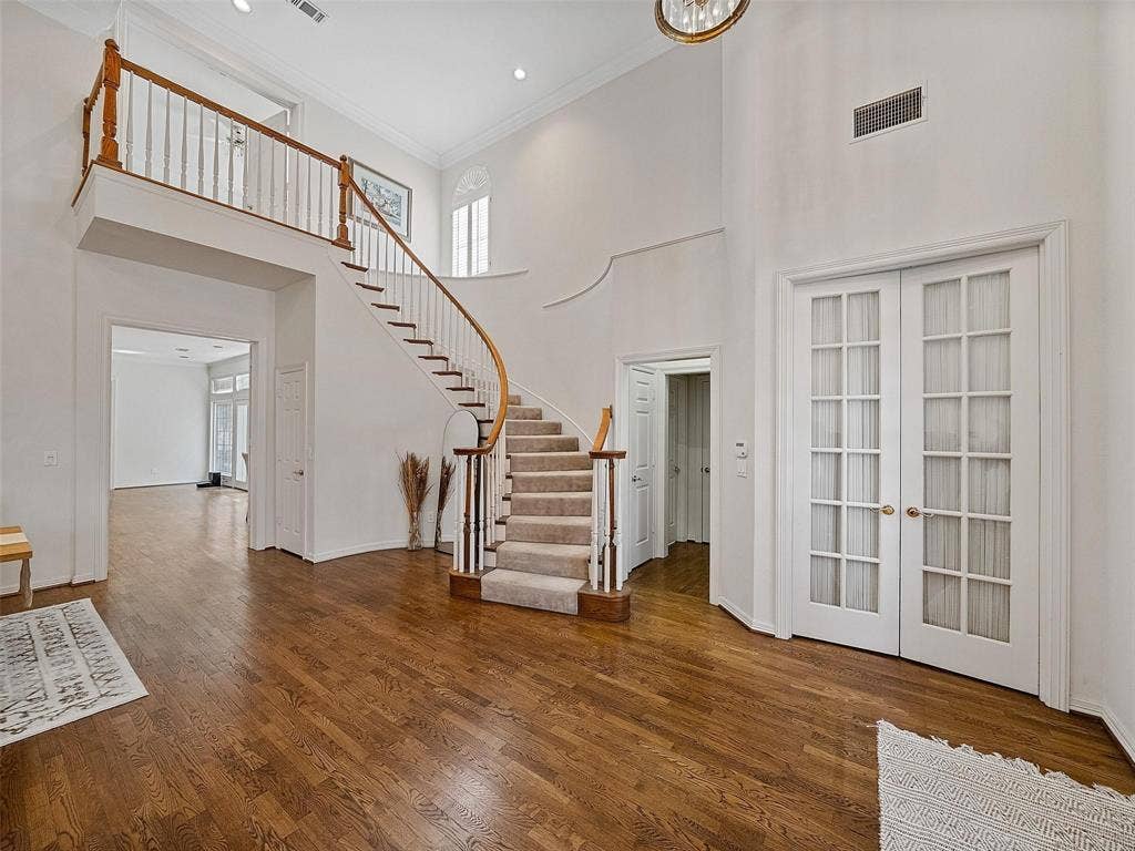 8640 Breakers Point, Dallas, TX 75243 Two-story foyer featuring a curved staircase with wood banister, wood-finish flooring, recessed lighting, and white French doors with brass hardware