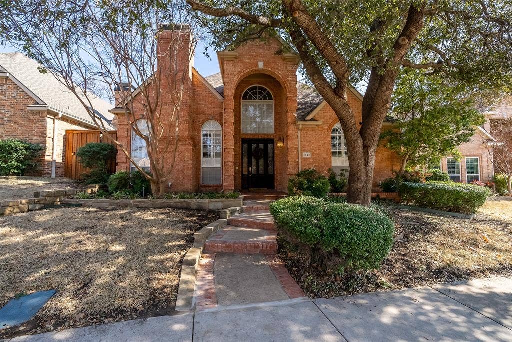 8640 Breakers Point, Dallas, TX 75243 Brick exterior with an arched entryway, transom window, and mature tree