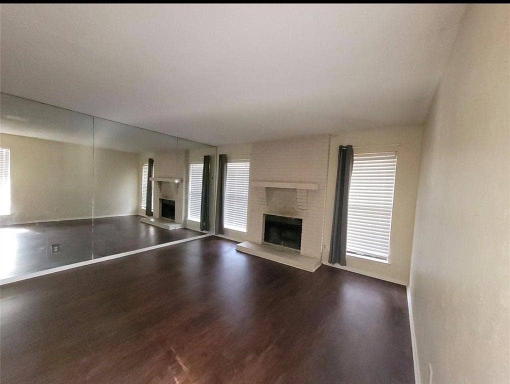 1801 W Spring Creek Parkway, #F2, Plano, TX 75023 Wood-finish flooring, full-wall mirrored accent, brick fireplace with a mantel, and multiple windows with blinds