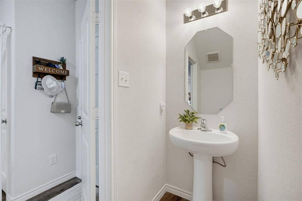 5525 Willamette Drive, Fort Worth, TX 76119 Pedestal sink with chrome faucet, classic octagonal mirror, and a three-light vanity fixture