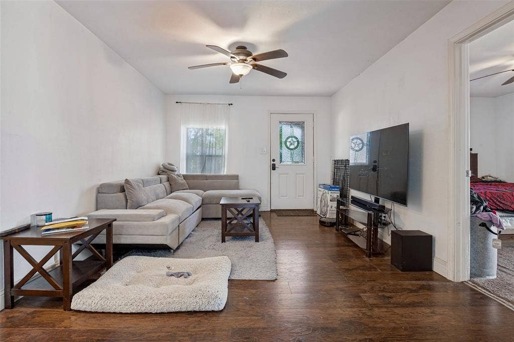 Wood-finish flooring throughout, white walls, and a ceiling fan with integrated lighting