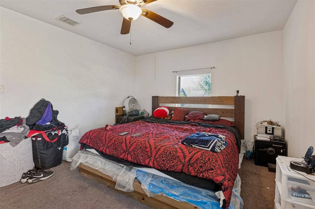 Carpeted flooring, white painted walls, ceiling fan with integrated lighting, and a window providing natural illumination