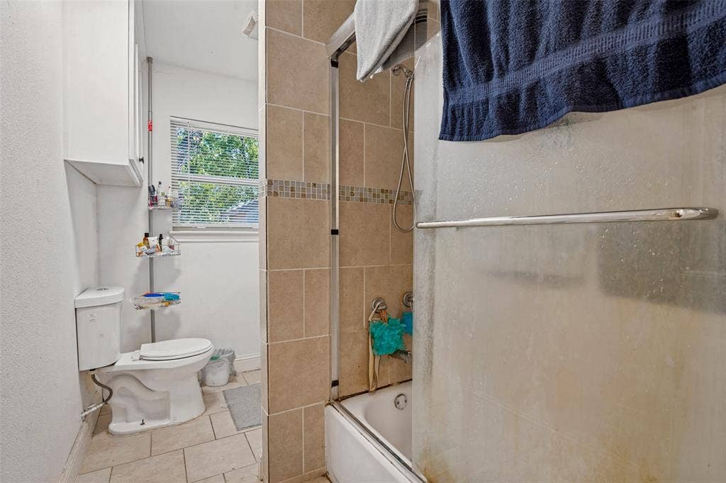Full bathroom featuring a shower-tub combination with tile surround, a toilet, a window with blinds, and tile flooring