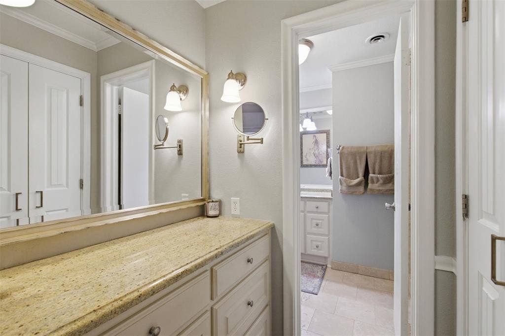 3612 Regent Drive, Dallas, TX 75229 Built-in vanity with a stone countertop, custom cabinetry, large wall mirror, and dual wall sconces
