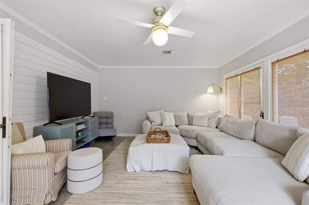 3612 Regent Drive, Dallas, TX 75229 Shiplap accent wall, crown molding, ceiling fan with integrated lighting, wood-finish flooring, and multiple windows with woven shades
