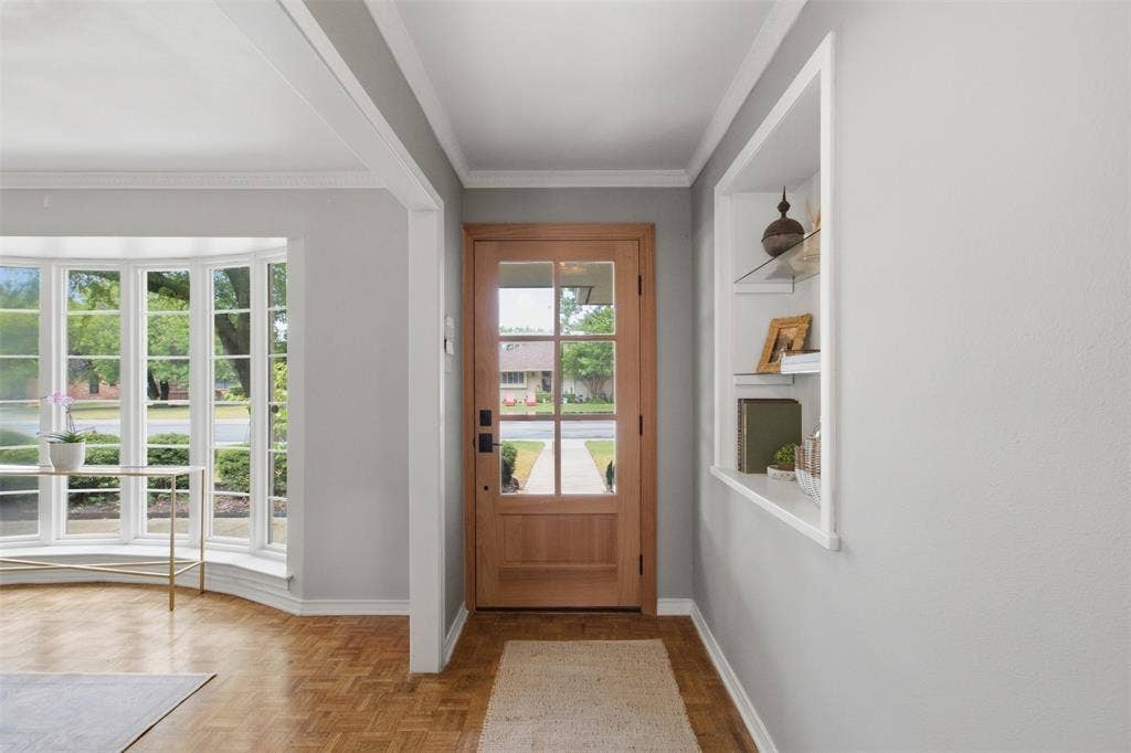 3612 Regent Drive, Dallas, TX 75229 Wood-finish parquet flooring, bay window with multiple panes, natural wood entry door with glass inserts, recessed built-in shelving, and crown molding details