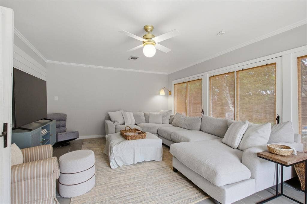 3612 Regent Drive, Dallas, TX 75229 Spacious living area featuring light gray walls, crown molding, a ceiling fan with integrated lighting, and multiple windows with natural wood blinds