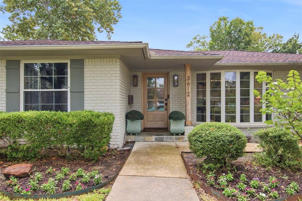 3612 Regent Drive, Dallas, TX 75229 White brick exterior with a wood-finish entry door, bay window, and decorative shutters