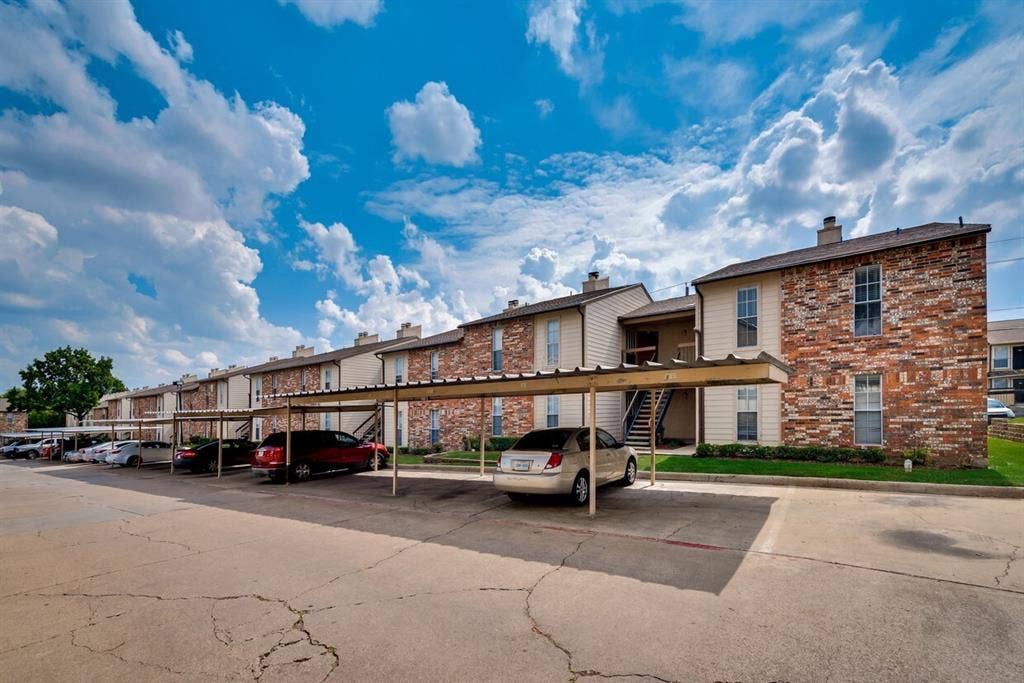 Multi-unit property with brick and siding exterior, featuring multiple covered parking spaces, and established landscaping