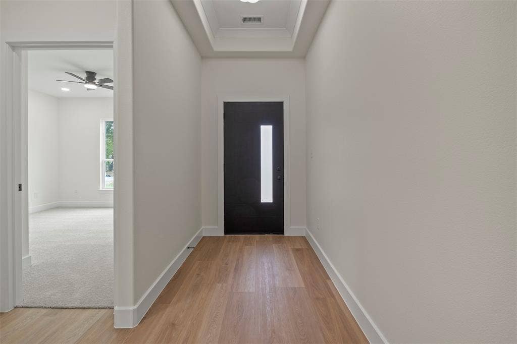 Recessed lighting, wood-finish flooring, tray ceiling, black front door with vertical pane, and light grey carpeting