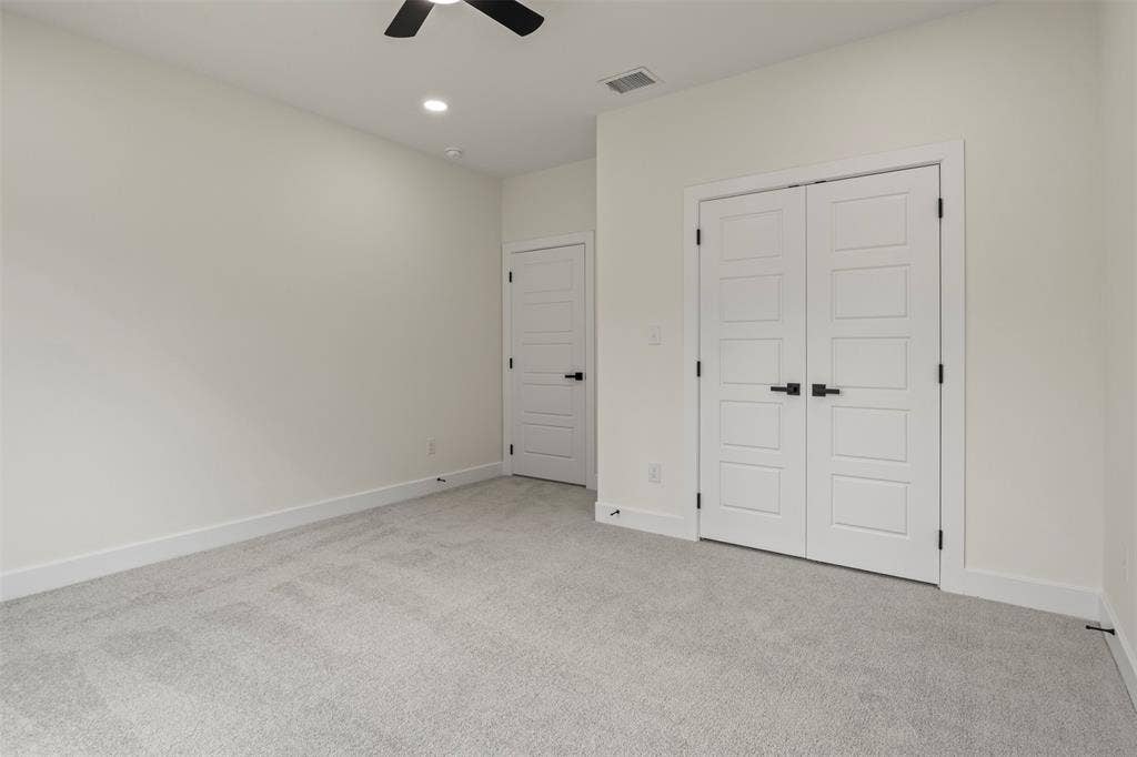 Light gray carpet flooring, white walls, two paneled doors with matte black hardware, and a ceiling fan with integrated lighting