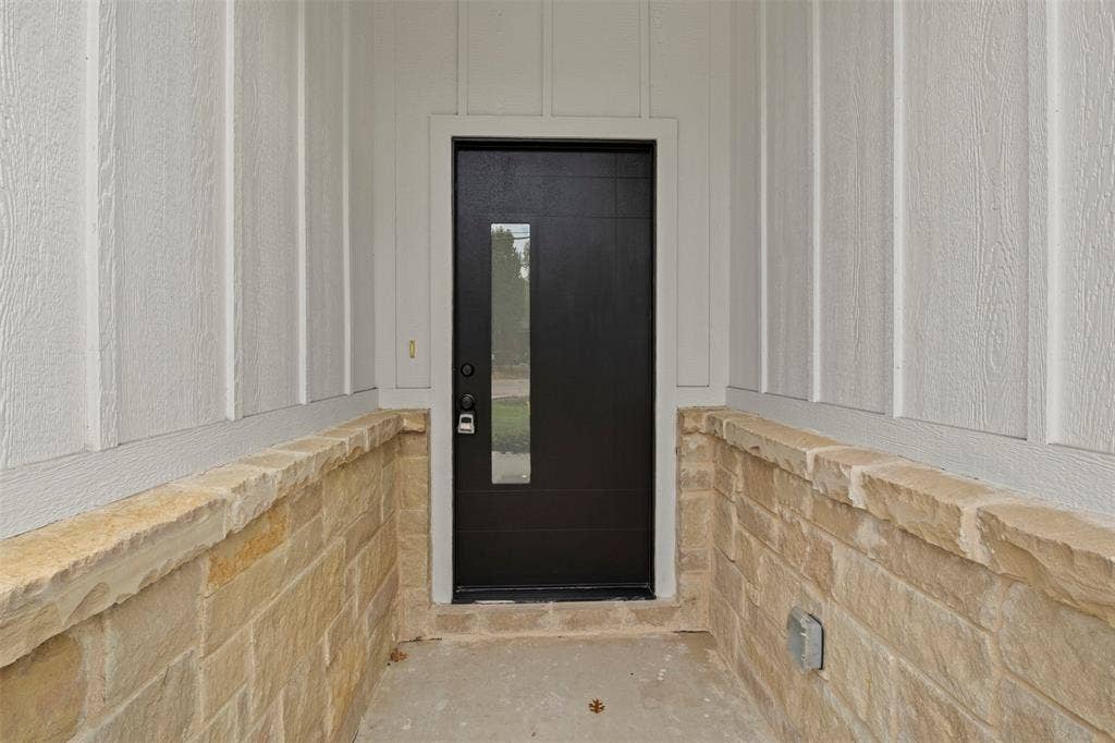 Board and batten siding with a stone veneer foundation and a contemporary dark entry door featuring a vertical privacy glass insert
