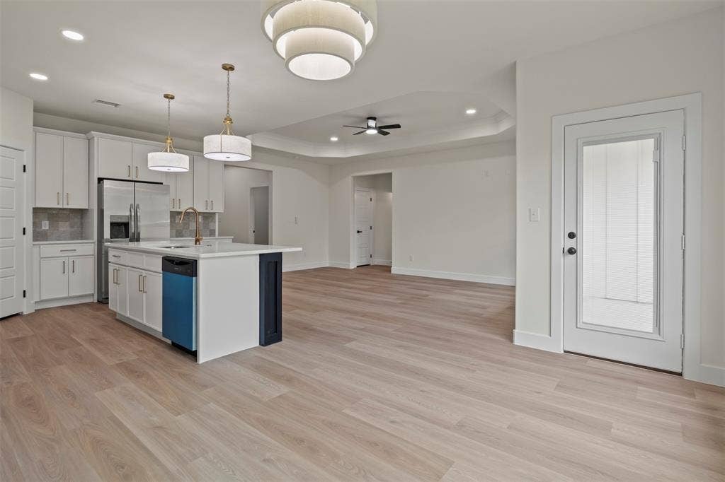 Modern kitchen featuring white cabinetry, a central island with a sink, stainless steel appliances, and wood-finish flooring throughout