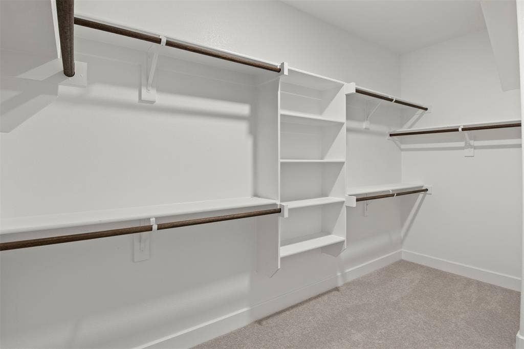 Walk-in closet featuring white built-in shelving, multiple hanging rods, and light-colored carpeting