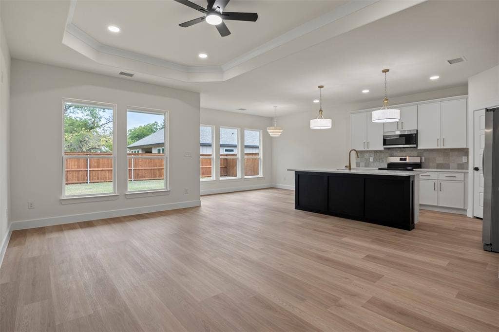 Open-concept living space featuring wood-finish flooring, recessed lighting, and a tray ceiling