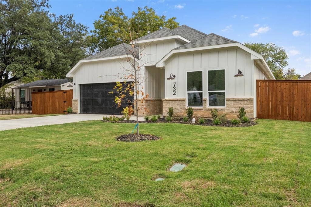 White board and batten siding, stone facade accents, dark garage door, concrete driveway, and a wood privacy fence