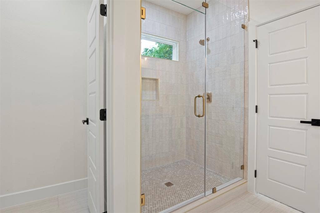 Glass-enclosed shower with gold-tone hardware, a tiled shower niche, and a window