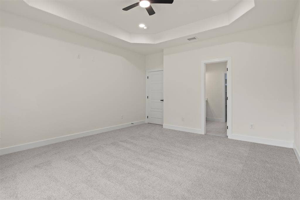 Tray ceiling with recessed lighting and a ceiling fan, light gray carpet flooring, and white trim