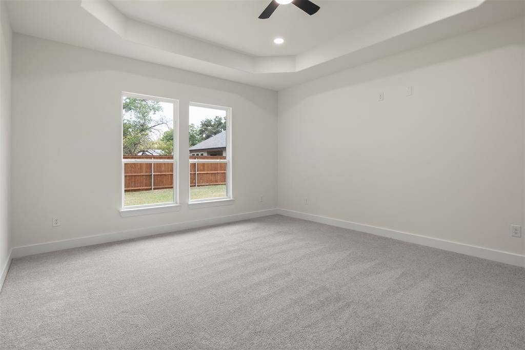 Tray ceiling with recessed lighting and a ceiling fan, two large windows, and neutral carpet