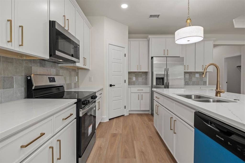 Modern kitchen featuring white cabinetry, gold-finish hardware, stainless steel appliances, light-toned countertops, and wood-finish flooring