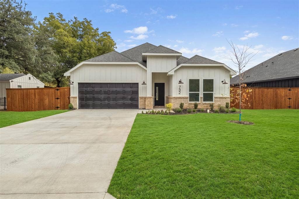 White board and batten siding with stone veneer accents, dark shingle roof, two-car garage with black door, concrete driveway, and front lawn