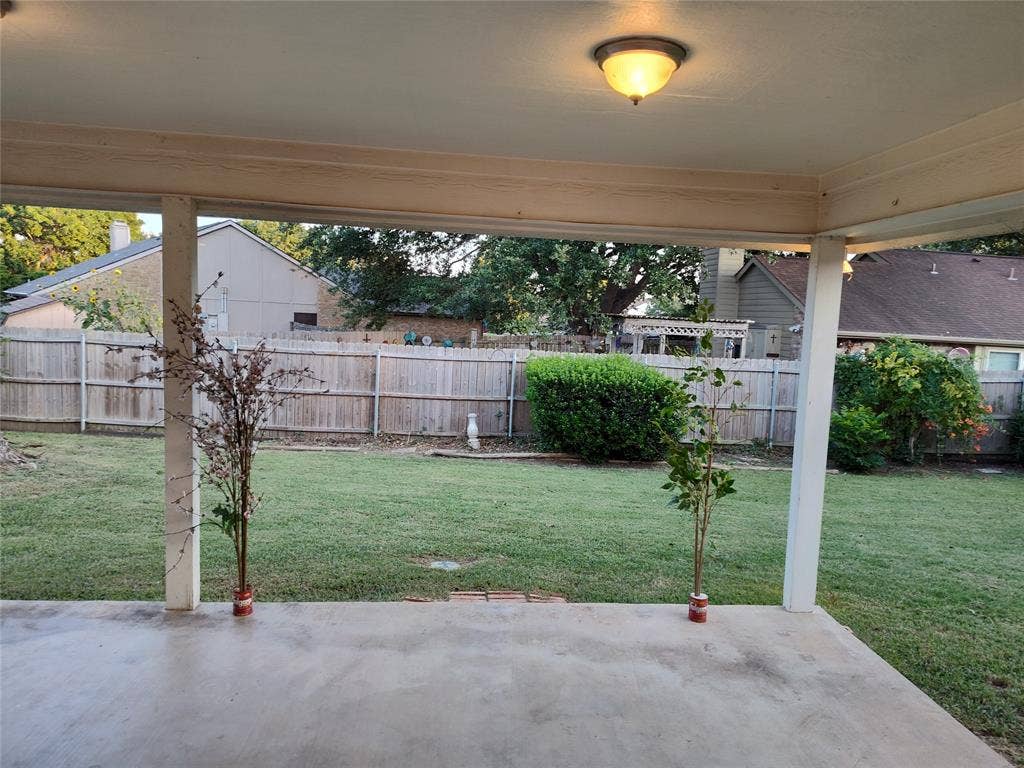 Covered concrete patio featuring a ceiling-mounted light fixture and wooden privacy fencing enclosing a grass lawn